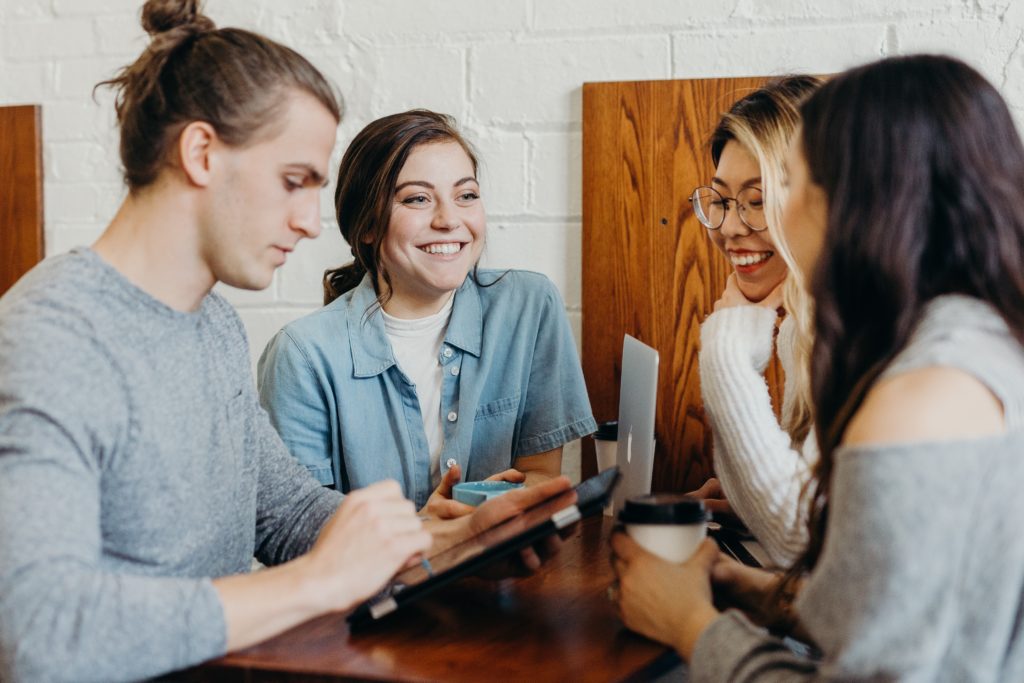 A man and three women with devices talking happily post-pandemic