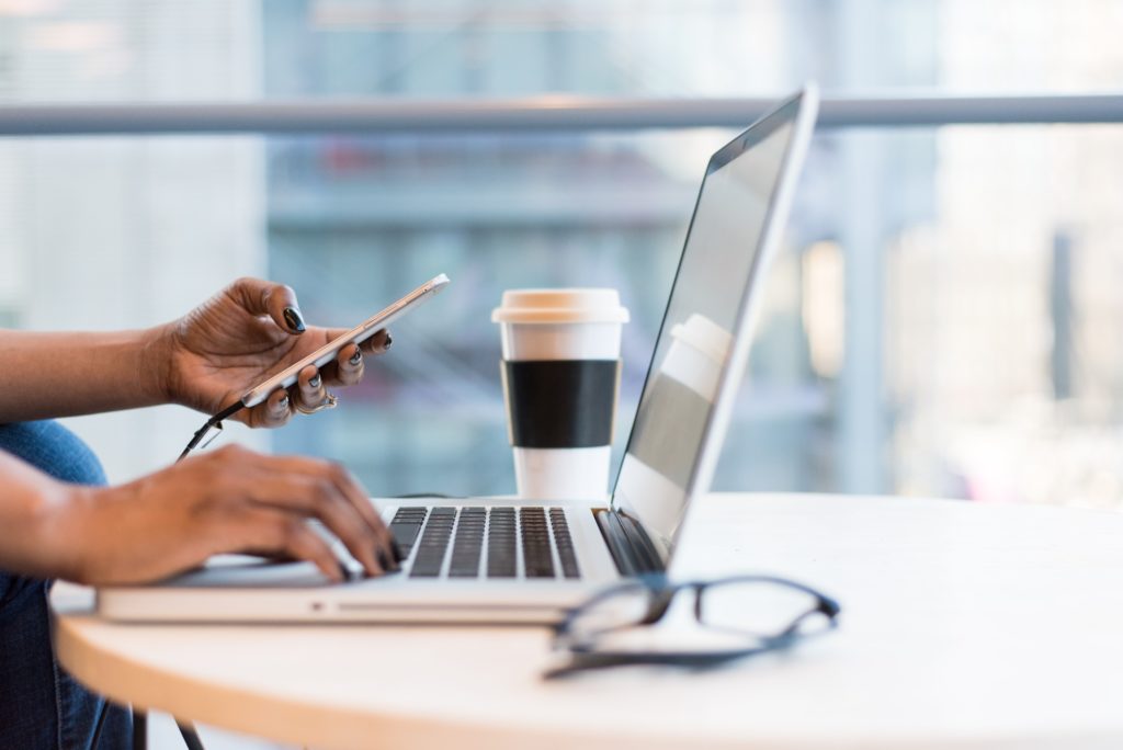 Hands typing on smartphone and laptop on desk