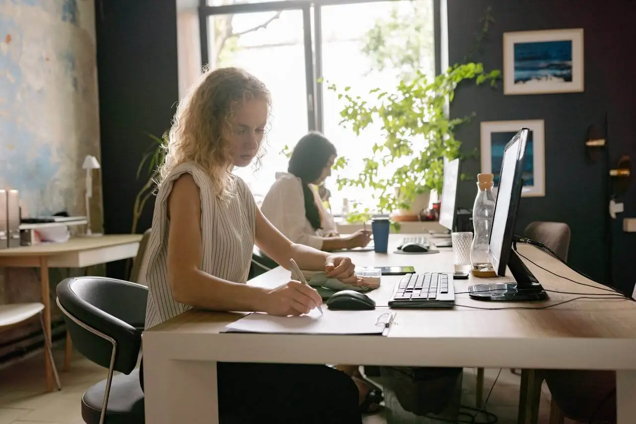 two-women-sitting-at-desk-on-computers Two women back in office following RTO mandate