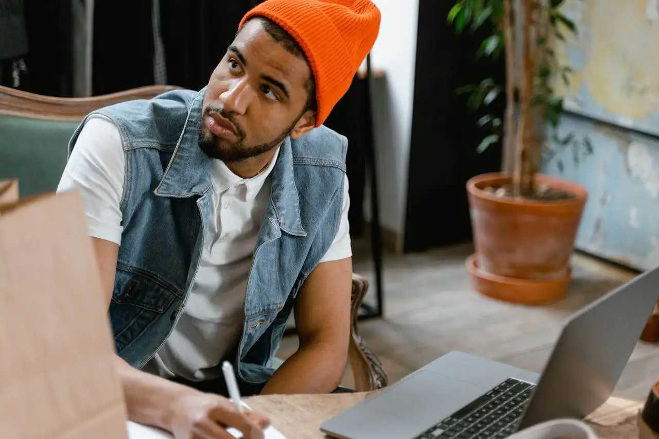 Man-in-Blue-Denim-Vest-and-Orange-Knit-Cap-Sitting-on-Chair Employee listening to manager feedback about his performance