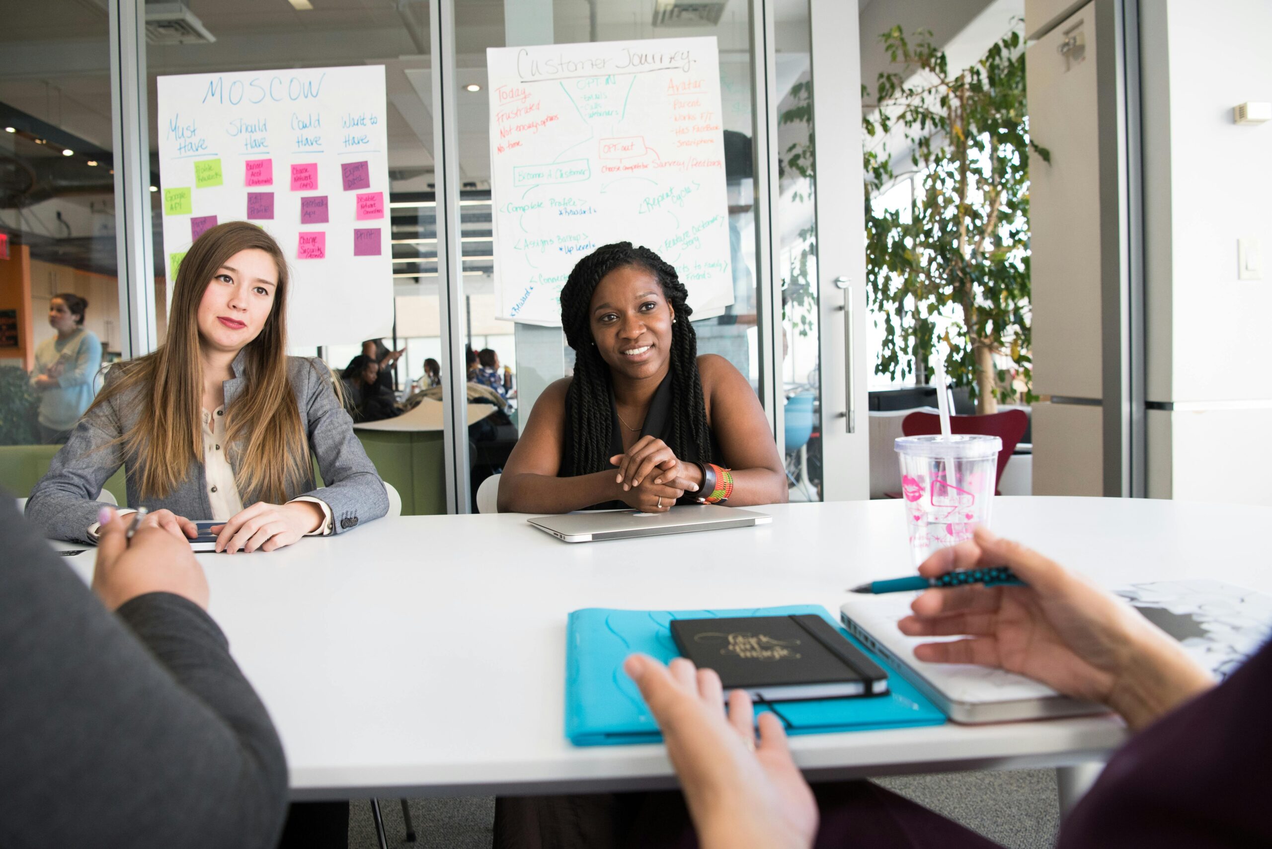 two-women-sitting-in-front-of-white-table HR managers meeting to discuss how to prevent workplace bullying.
