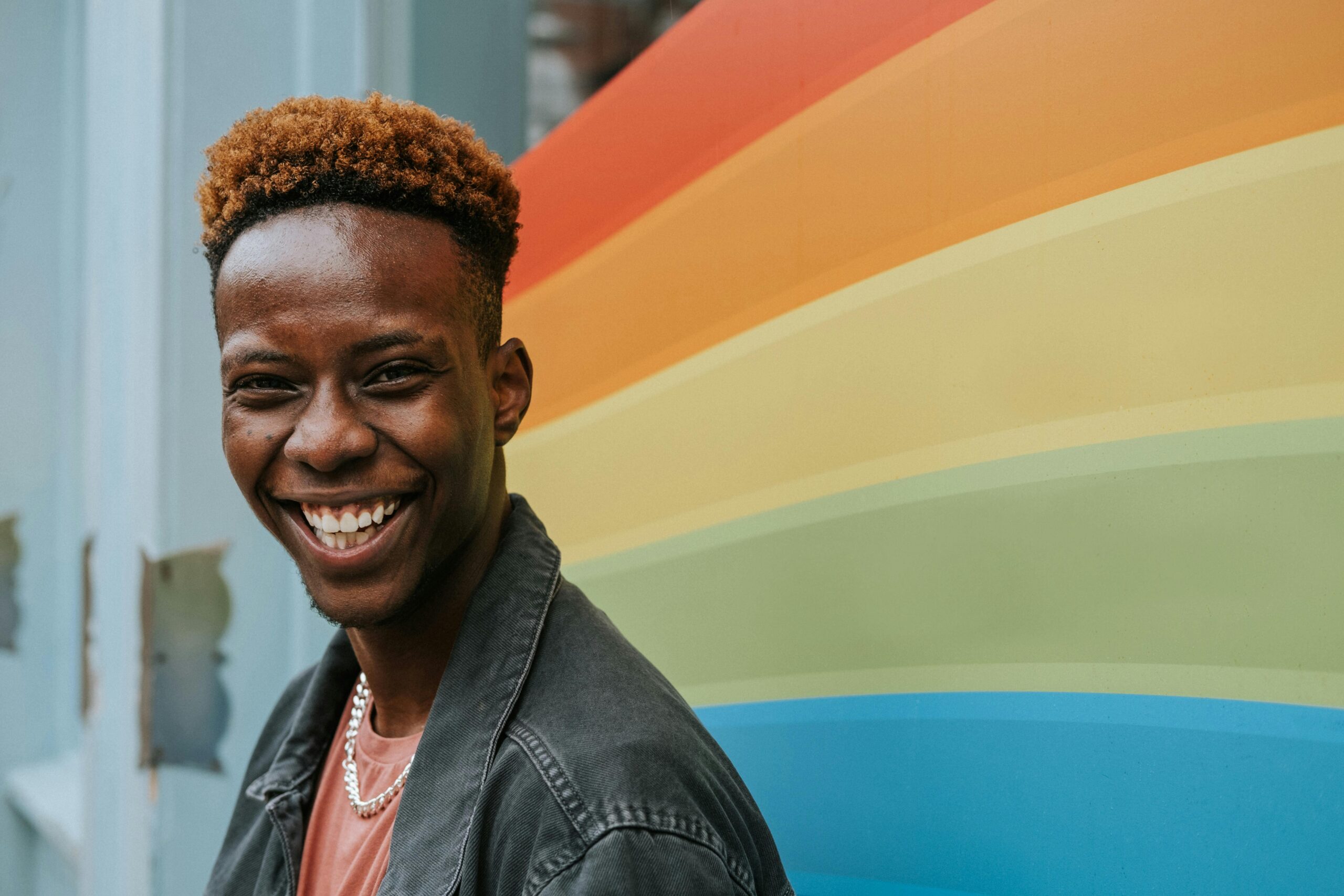 positive-young-black-guy-laughing-near-graffiti-wall-with-rainbow-flag A young man participating in a gay pride