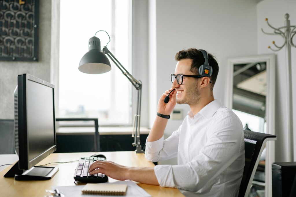 A man sitting at his computer, answering calls while smiling
