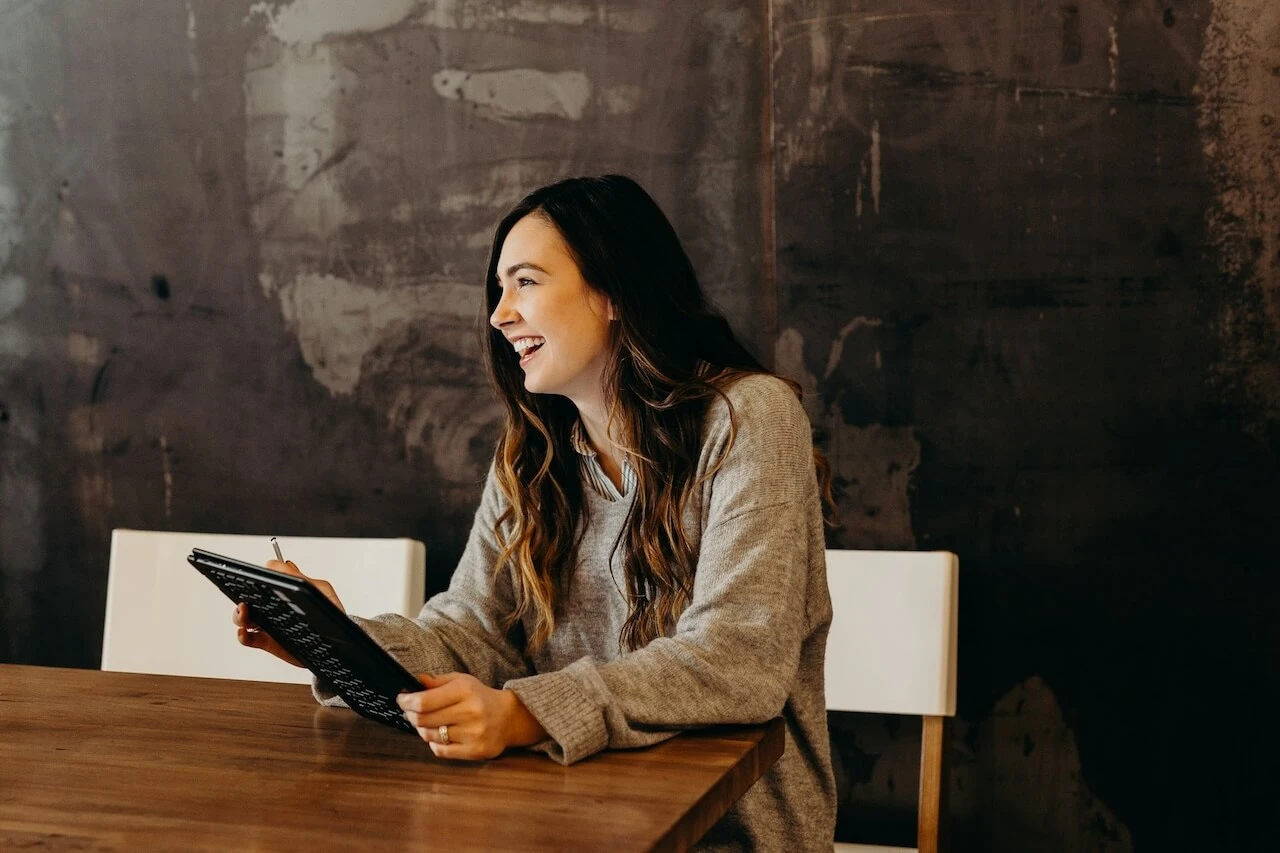 woman-smiling-sitting-around-table-holding-tablet Improve retention with happy employees